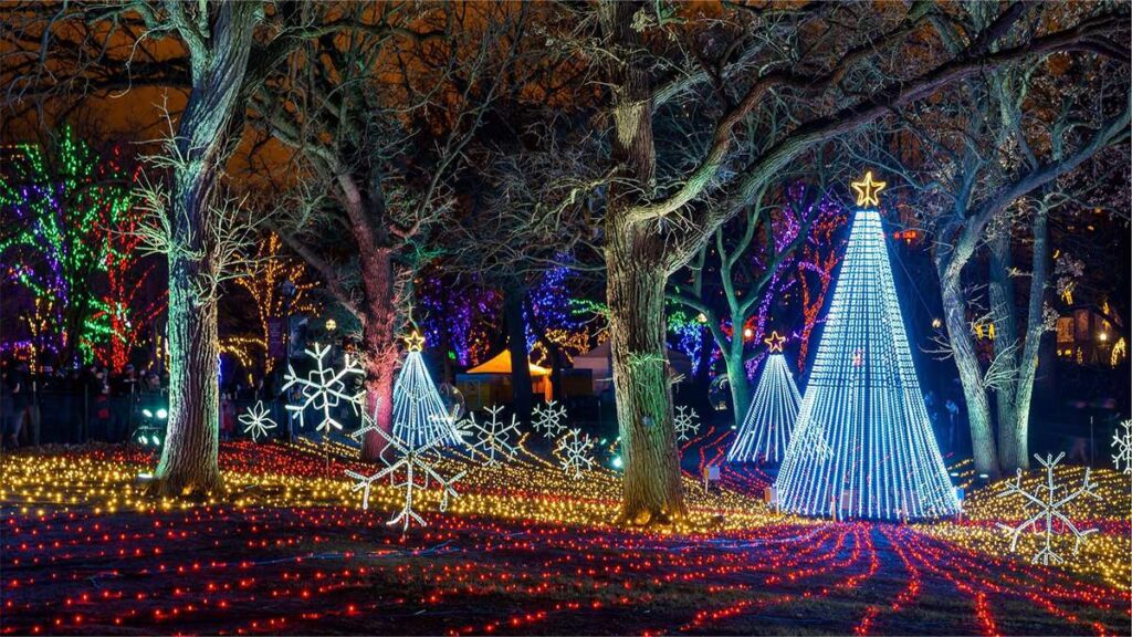 Colorful Christmas lights illuminate a festive outdoor scene with decorated trees and snowflakes.
